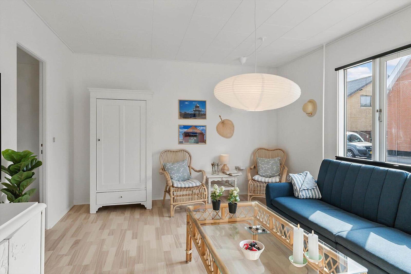 Living room with blue sofa, two rattan chairs, and glass table.