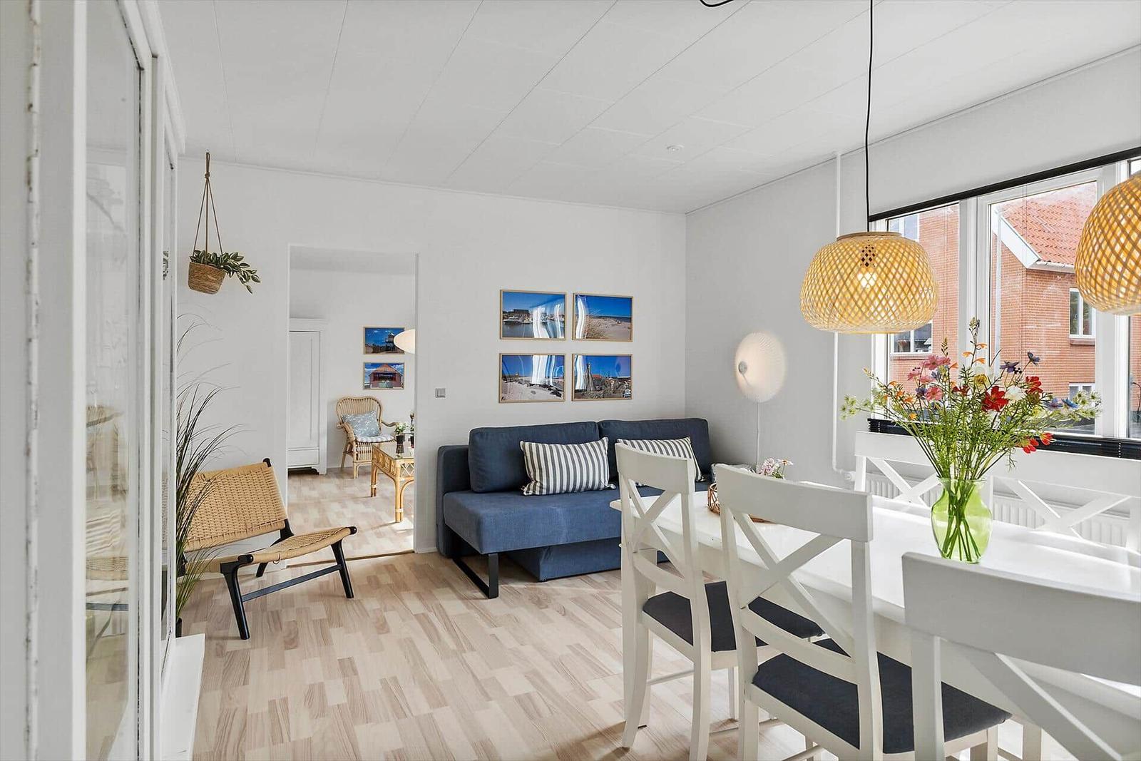 Living and dining area with blue sofa, white table and chairs, wall pictures and hanging plants.