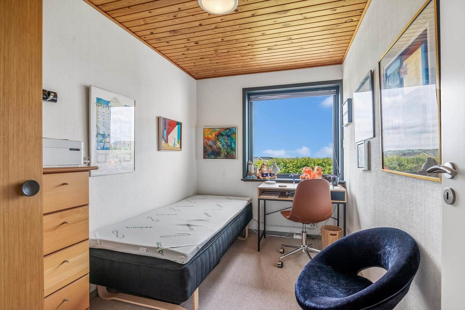 Schlafzimmer mit Bett, Schreibtisch und Stuhl. Holzdecke und Fenster mit Blick.