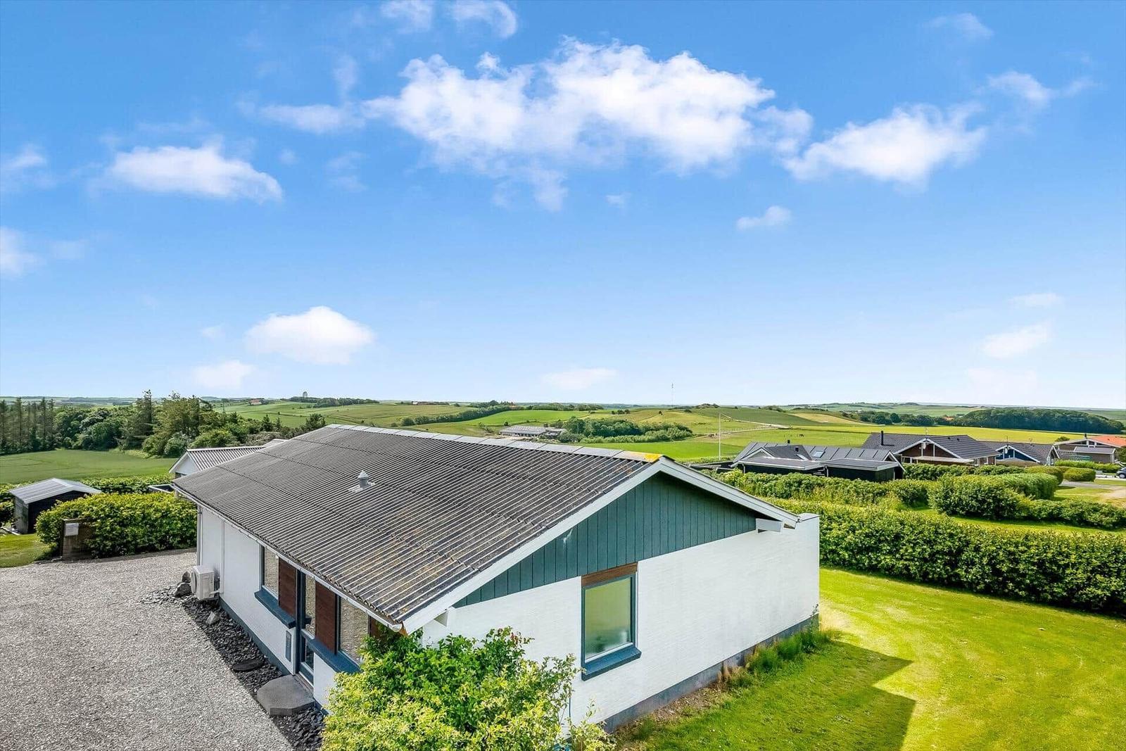Modernes Haus mit grünem Garten und Blick auf Felder unter blauem Himmel.