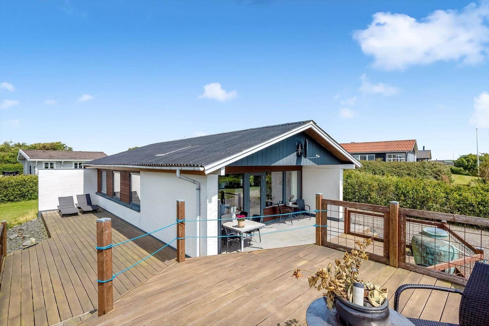 Modernes Ferienhaus mit großem Holzterrasse und Gartenbereich.