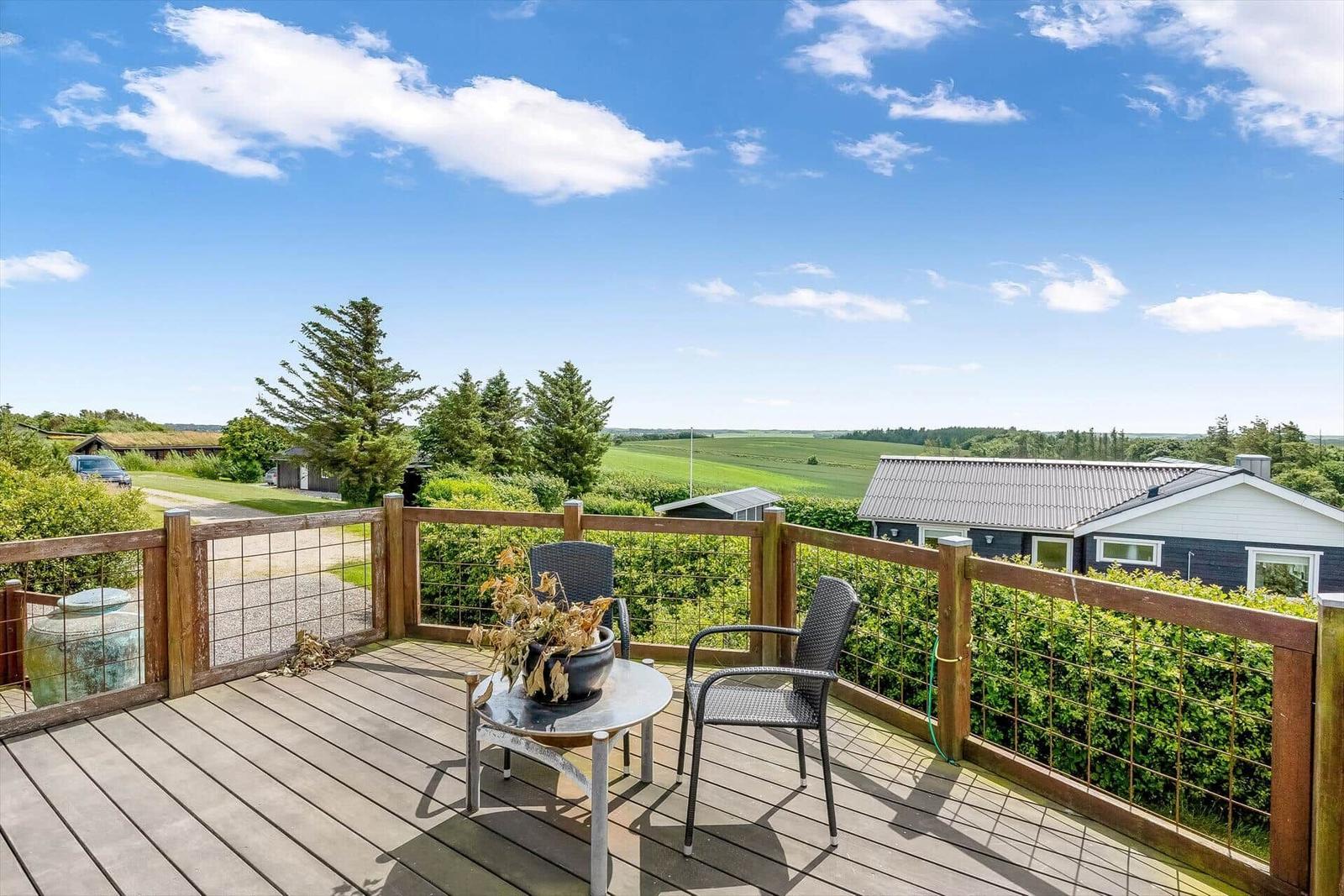 Terrasse mit Tisch und Stühlen, Blick auf grüne Landschaft und Häuser.