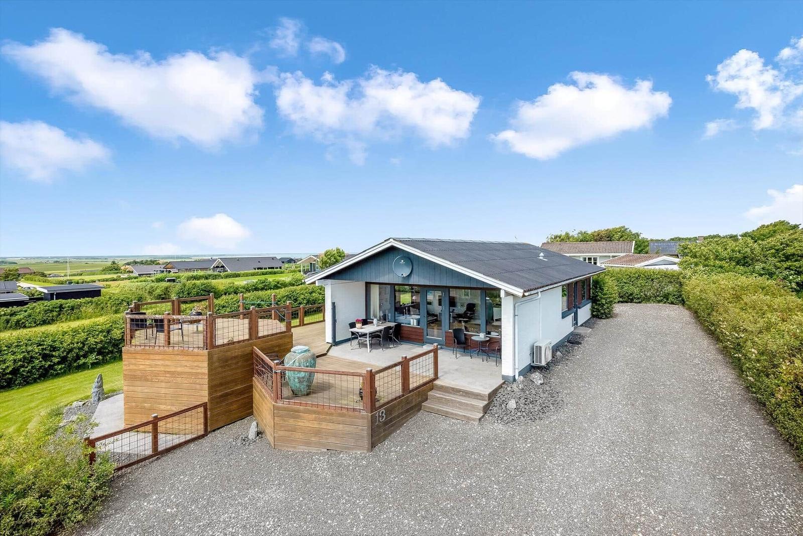 Moderne Ferienhaus mit Terrasse und Blick auf grüne Landschaft unter blauem Himmel.