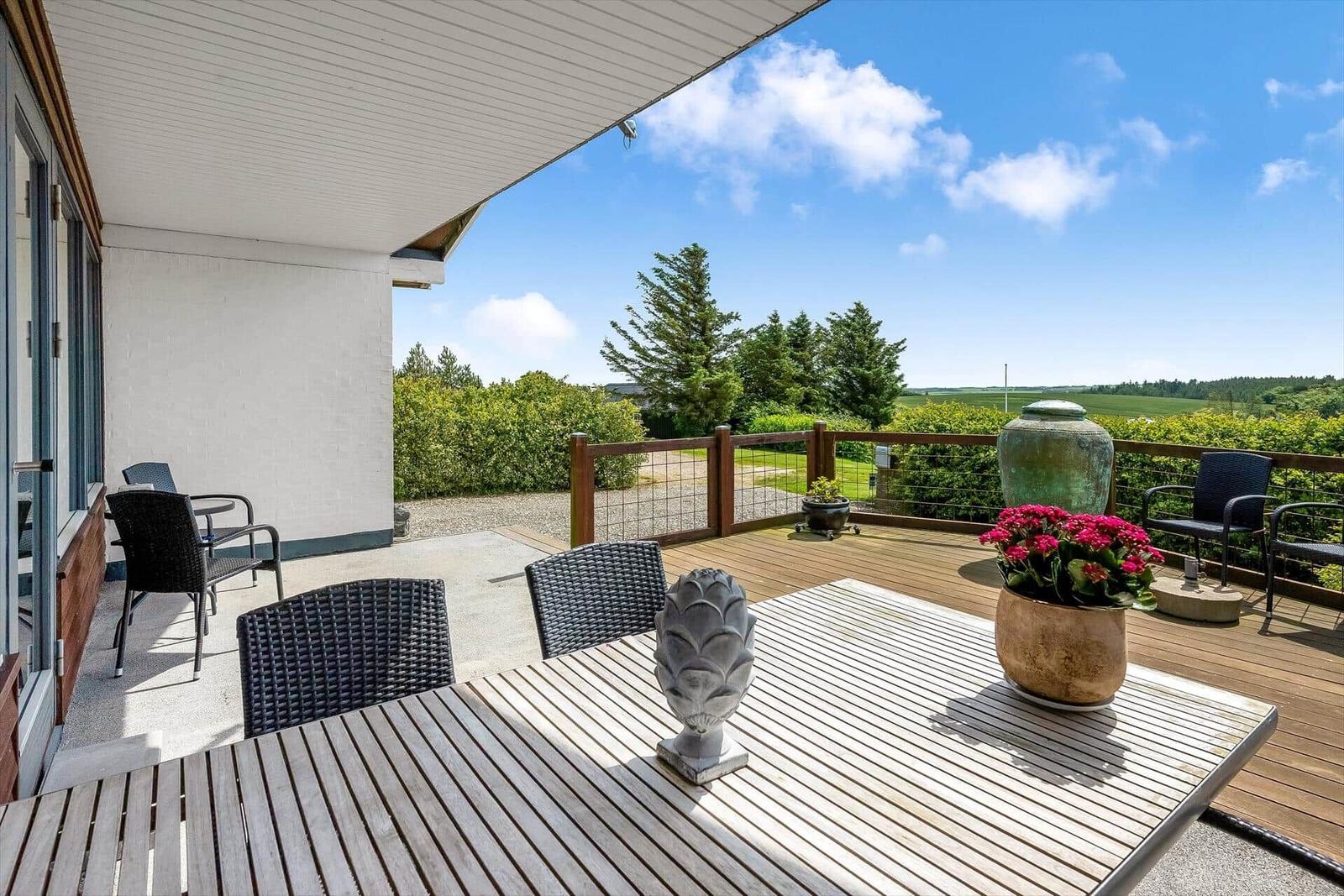 Terrasse mit Tisch, Stühlen und Blick auf grüne Landschaft.