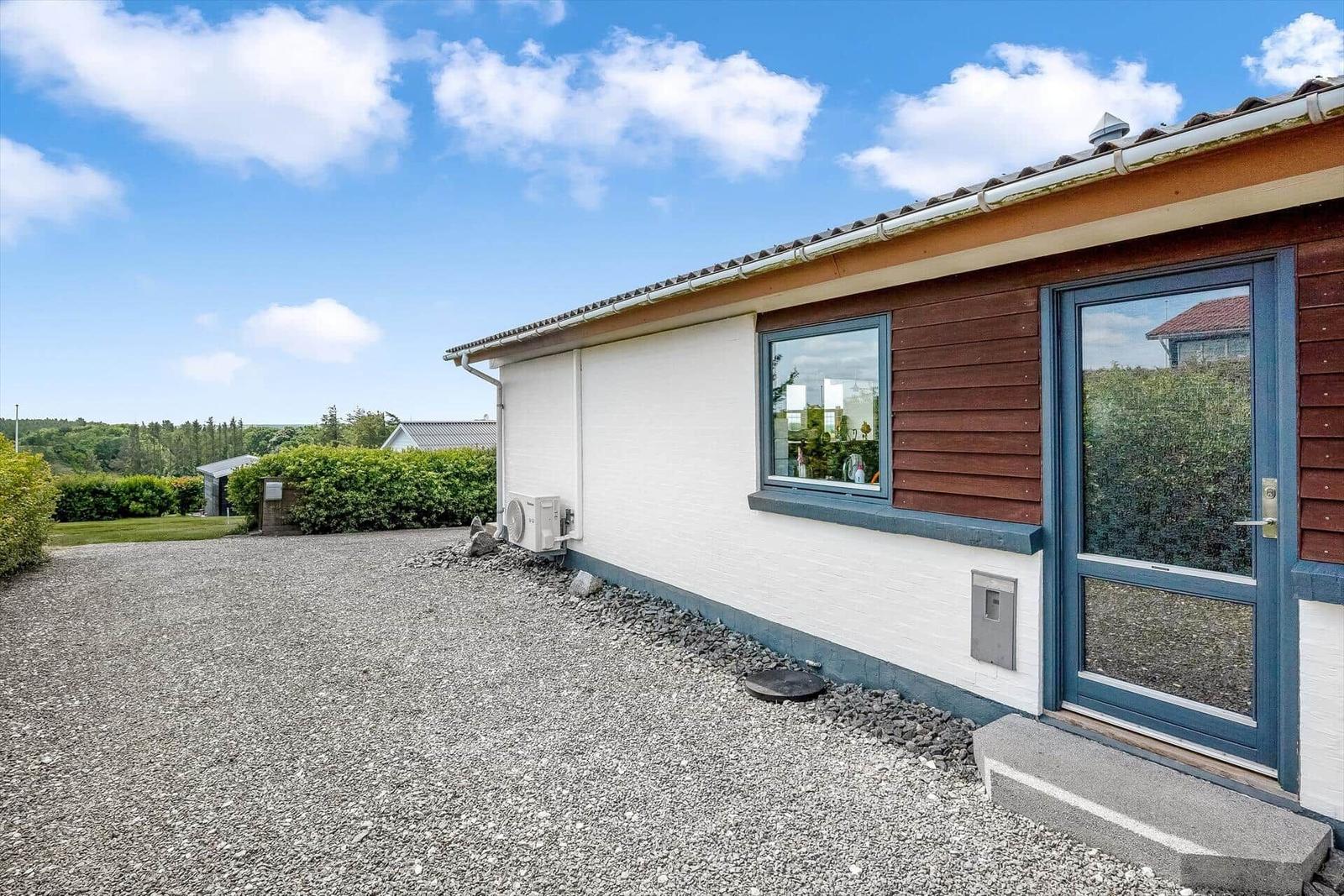 Moderne Ferienwohnung mit Holzfassade und Kiesvorplatz unter blauem Himmel.