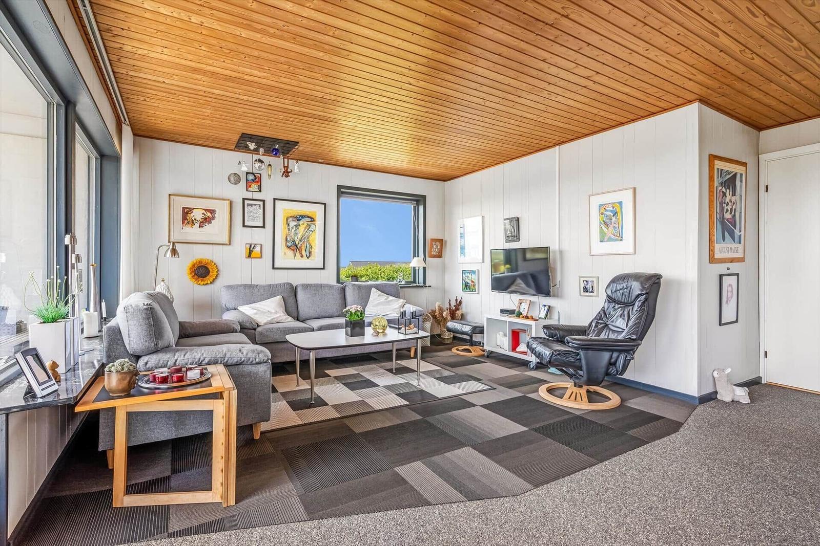 Wohnzimmer mit grauem Sofa, schwarzem Sessel und Holzdecke.
