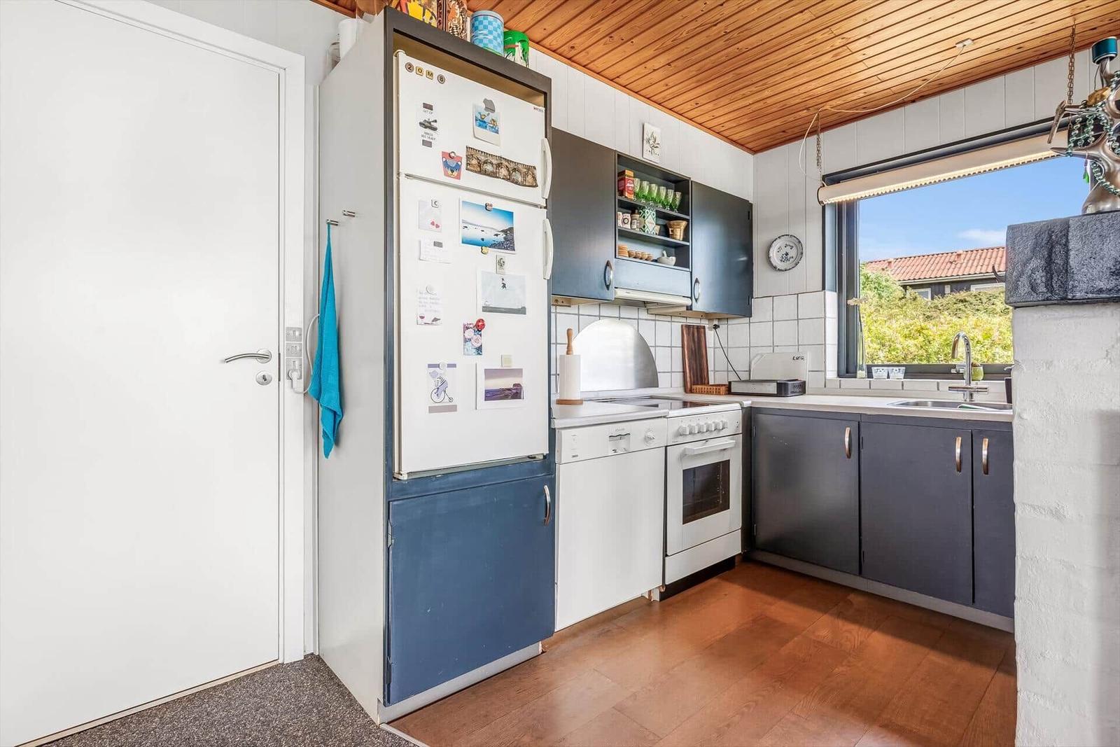Küche mit Kühlschrank, Spüle und Fenster. Holzdecke und Boden.