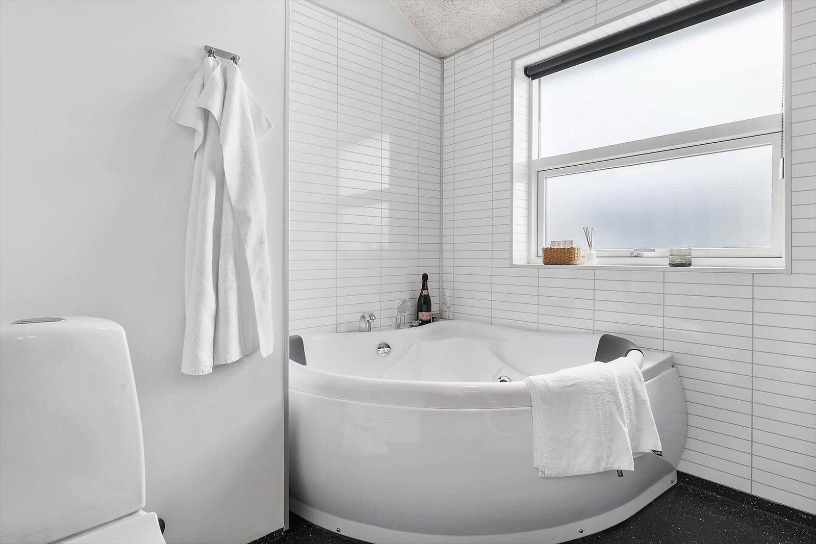Bad mit Eckbadewanne, Fenster und weißen Fliesen.