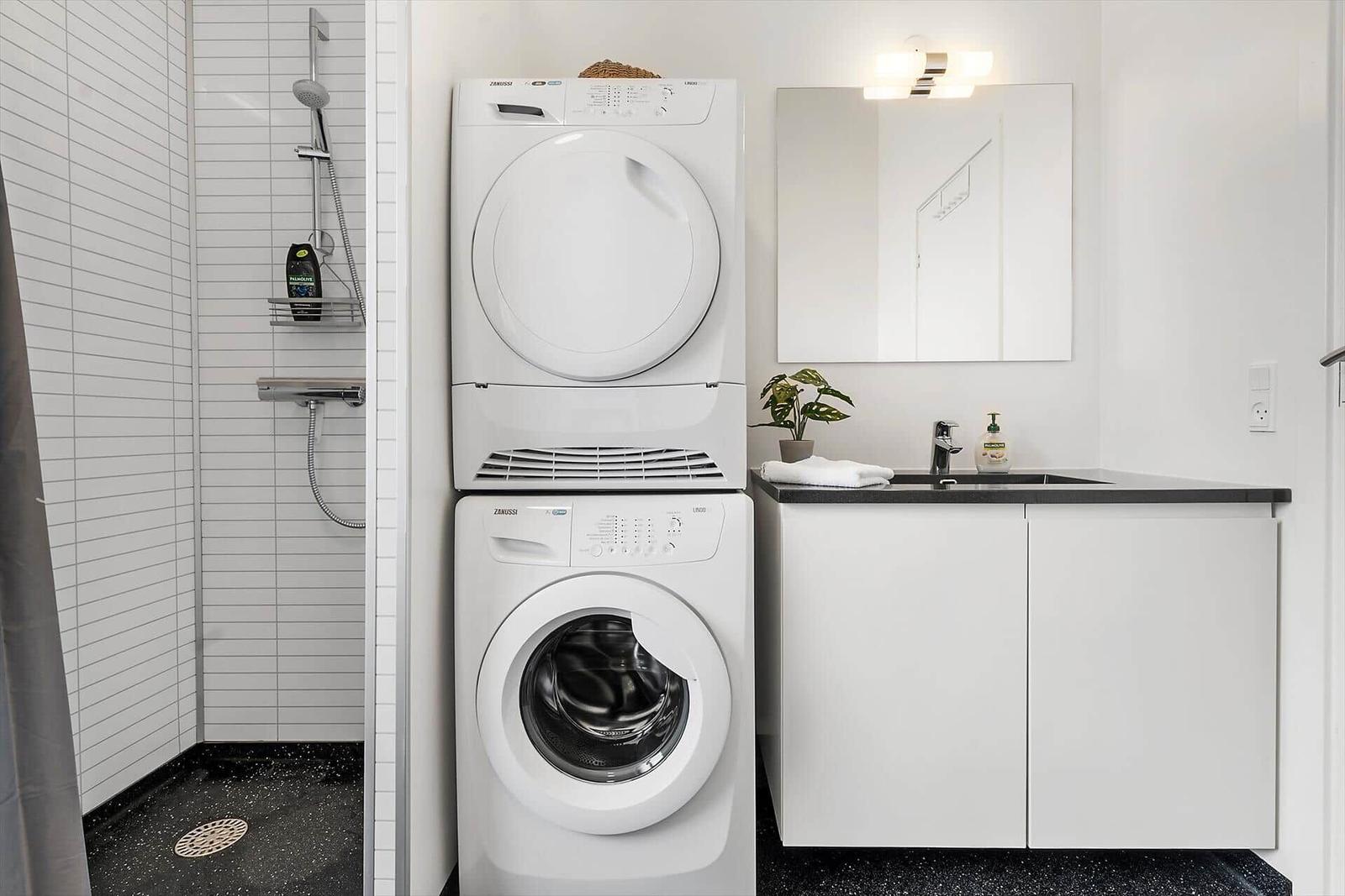 Waschmaschine und Trockner stehen in einem Badezimmer mit Dusche und Waschbecken.