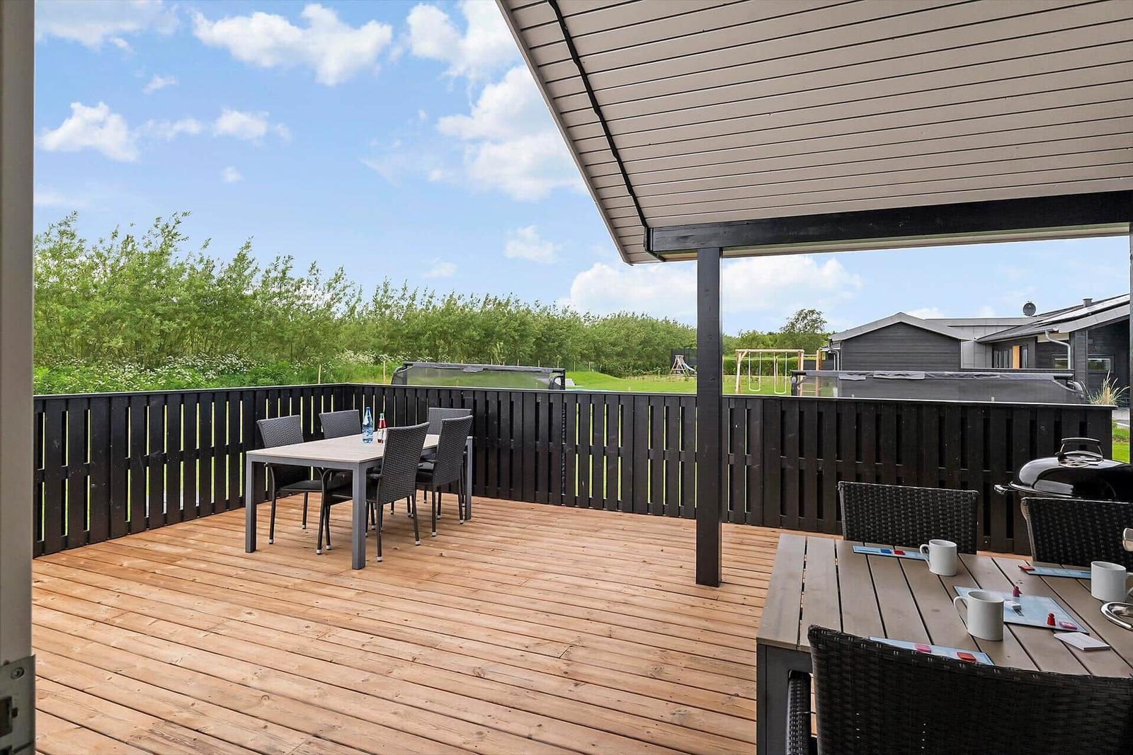 Terrasse mit Tischen, Stühlen und Grill. Blick auf Grünflächen und Nachbarhäuser.