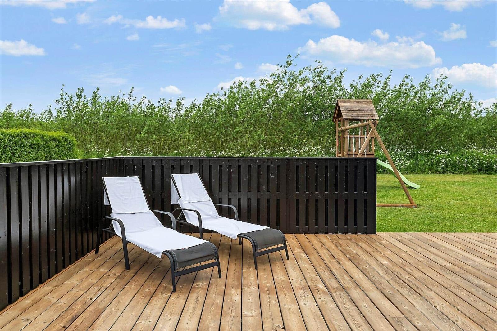 Terrasse mit zwei Liegestühlen, Holzdecke und Spielhaus im Hintergrund.