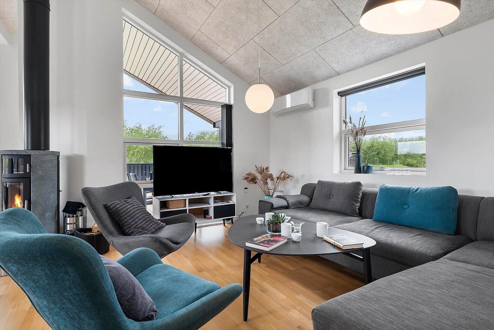 Wohnzimmer mit Sofa, Sessel und Kamin. Große Fenster und Holzboden.
