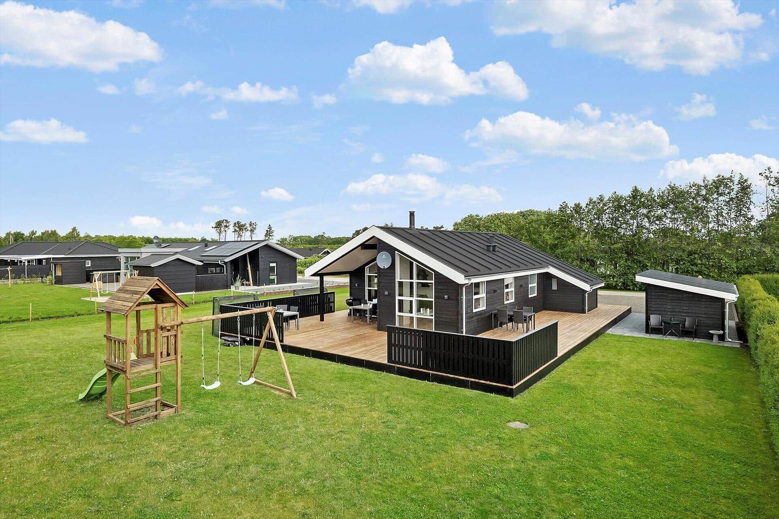 Schwarze Holzhütte mit großem Balkon und Spielplatz auf grünem Grundstück.