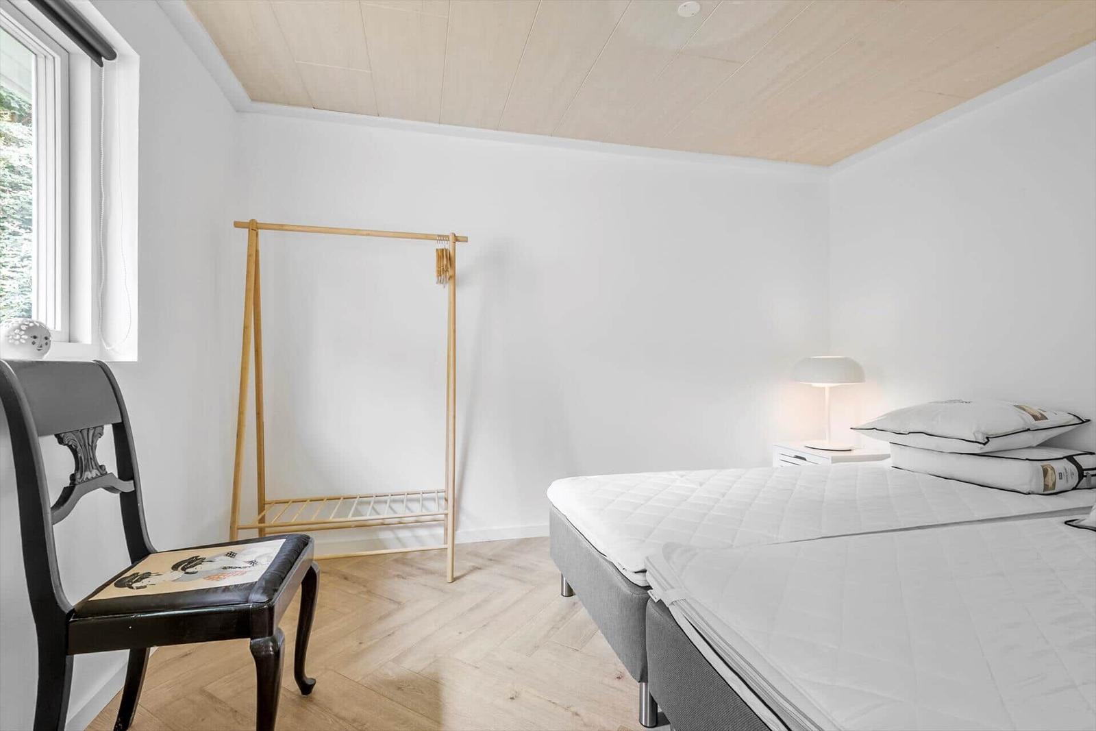 Schlafzimmer mit Bett, Kleiderständer und Stuhl an Fenster