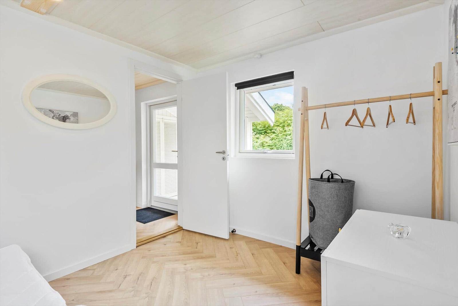 Zimmer mit Holzboden, Kleiderständer und Fenster mit Blick auf Grün.