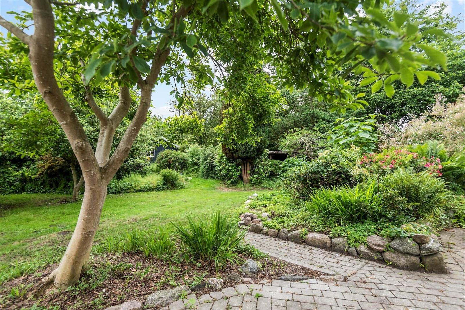 Garten mit gepflasterter Weg, Bäumen und Blumenbeeten.