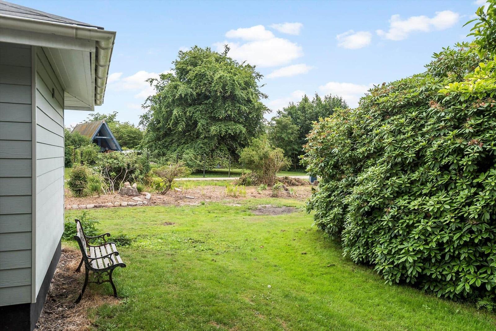Grüner Garten mit Bank, Sträuchern und Baum. Hausansicht mit Dach und Wand.