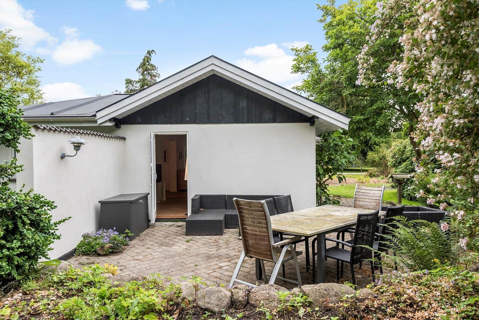 Haus mit Terrasse, Gartenmöbel und blühenden Sträuchern.