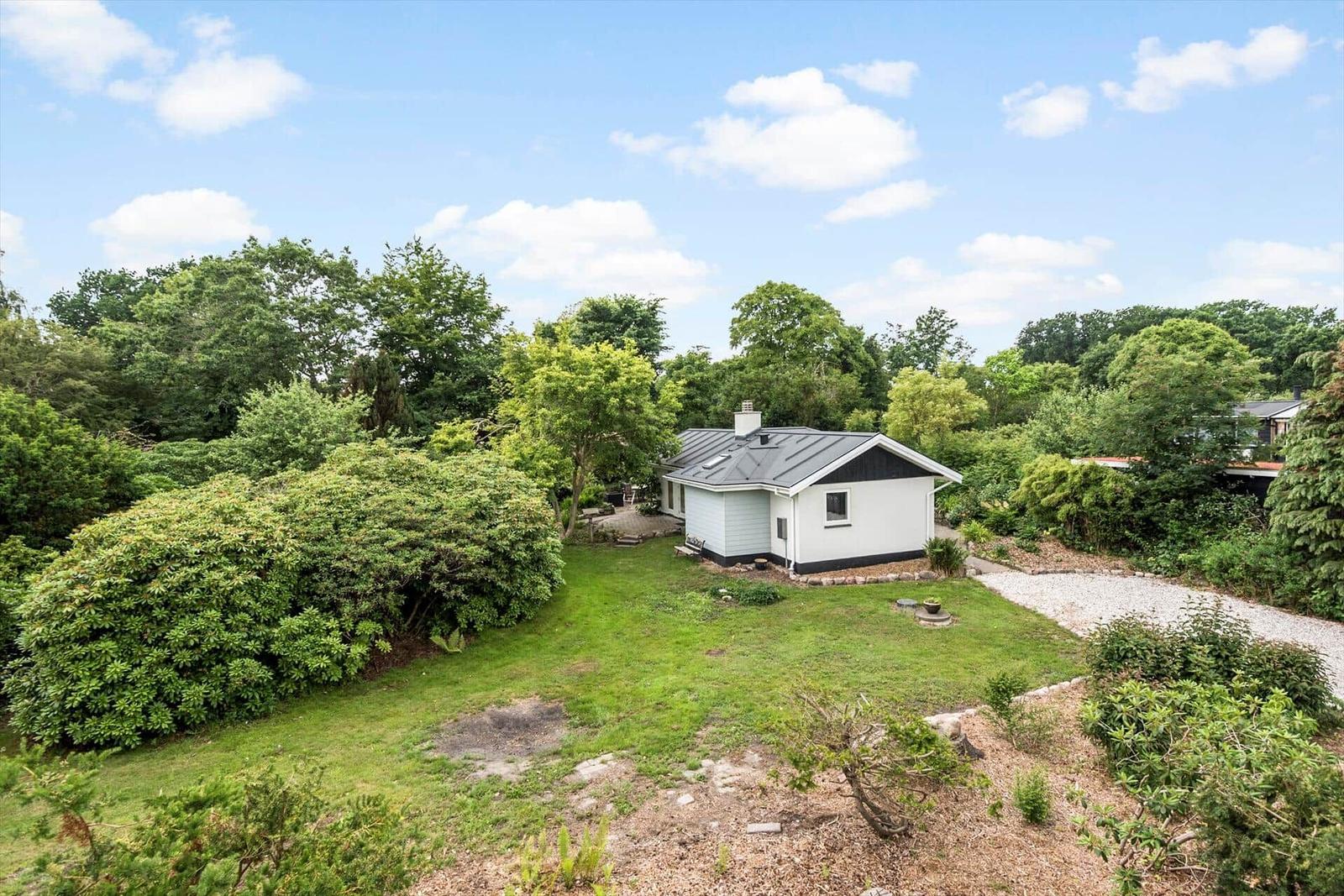 Wohnhaus mit Garten und Wald im Hintergrund unter blauem Himmel.