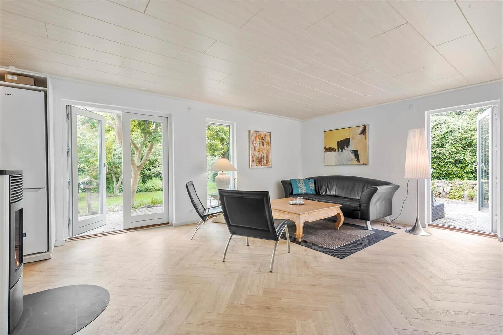 Wohnzimmer mit Sofa, Tisch und Stühlen. Holzfußboden und Fenster zur Außenterrasse.