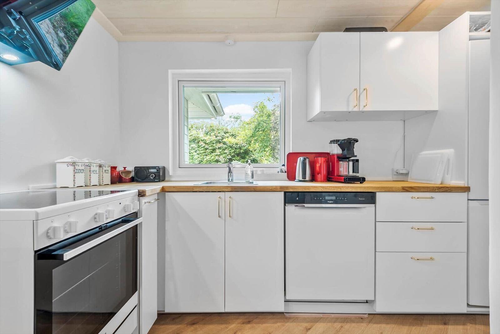 Küche mit weißen Schränken, Holzoberfläche und Fenster zum Garten.