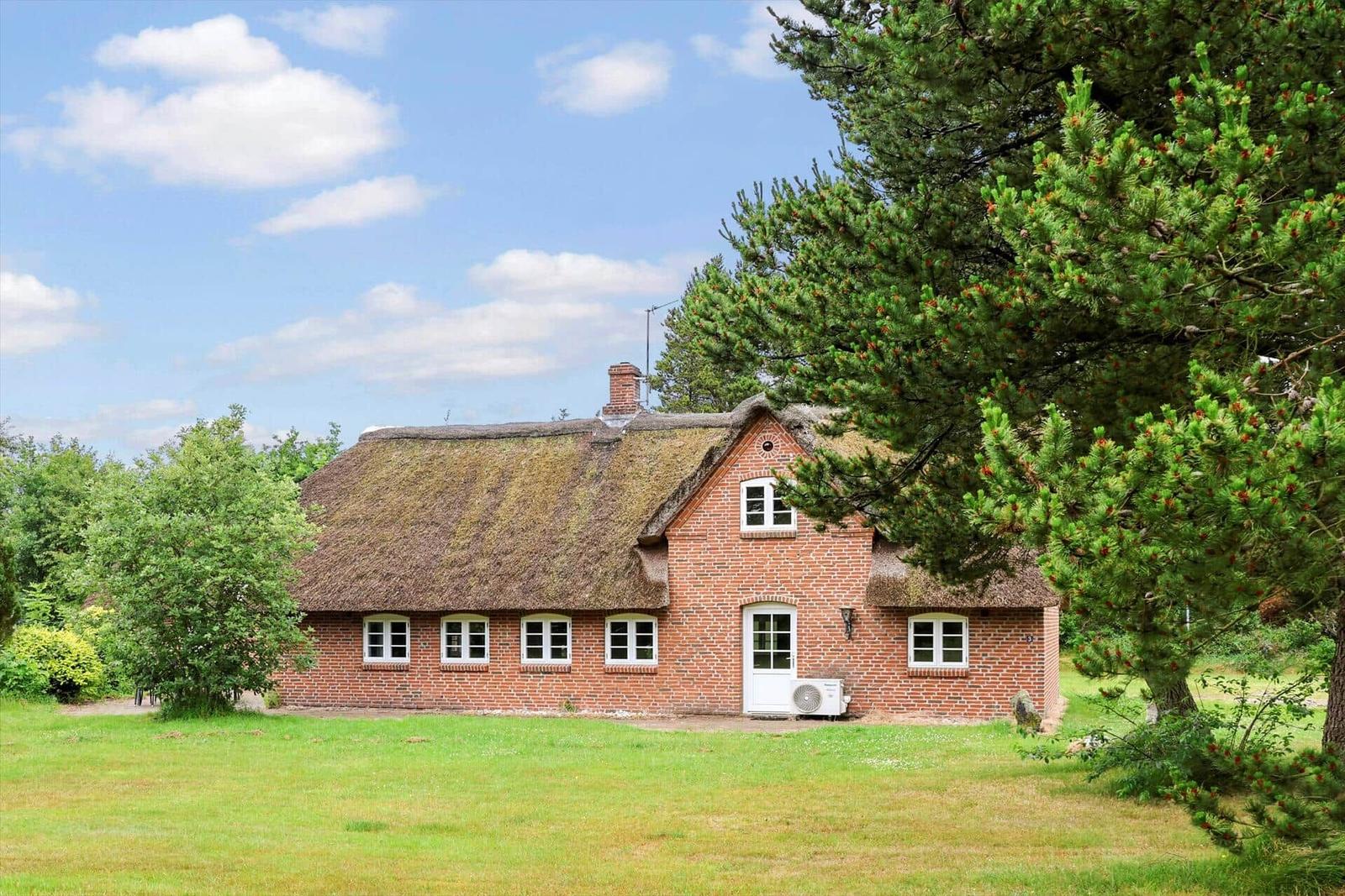 Rotes Backsteingebäude mit strohgedecktem Dach und weißen Fenstern in grüner Umgebung.