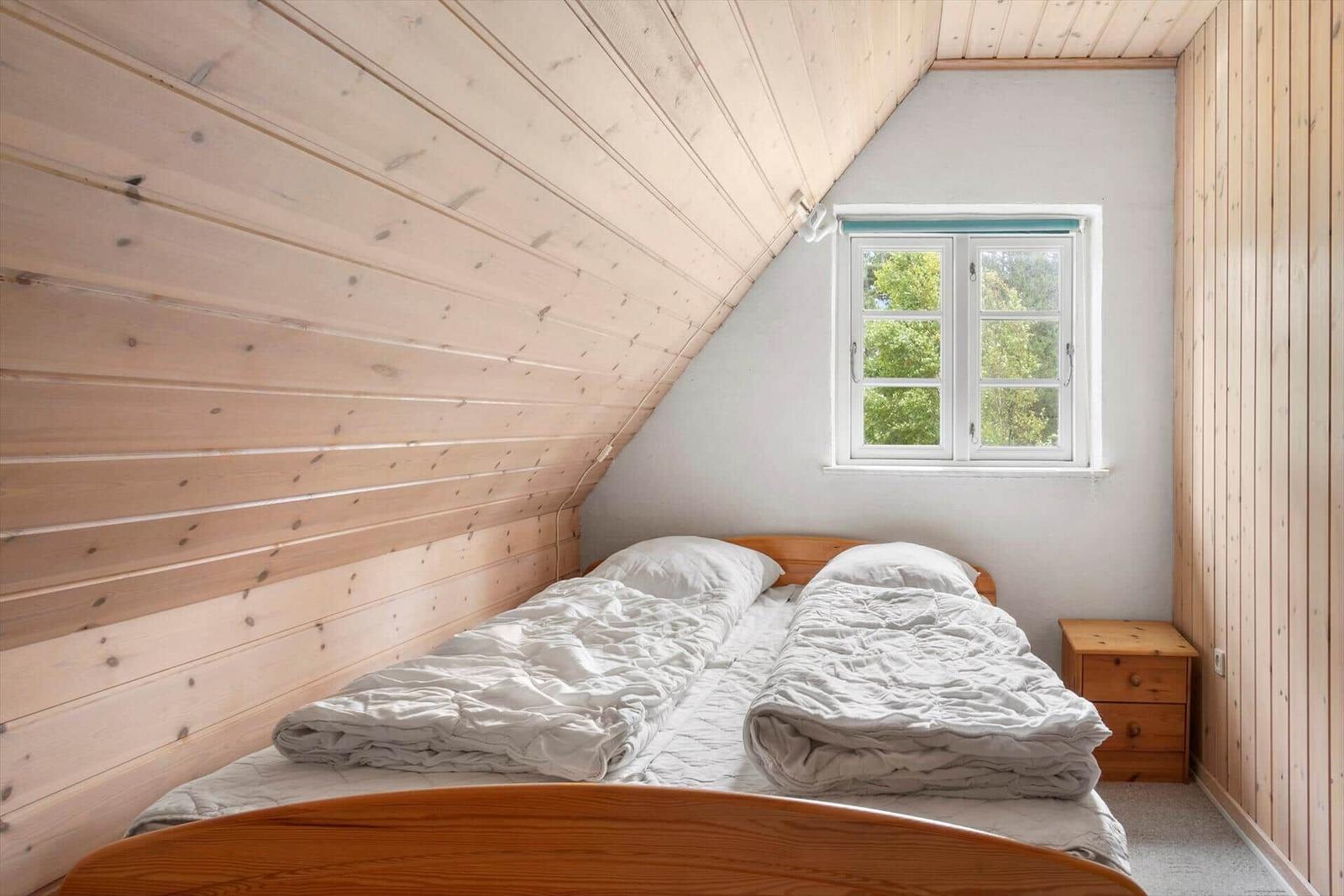Schlafzimmer mit Dachschrägen, Holzwänden und Fenster mit Blick auf Bäume.