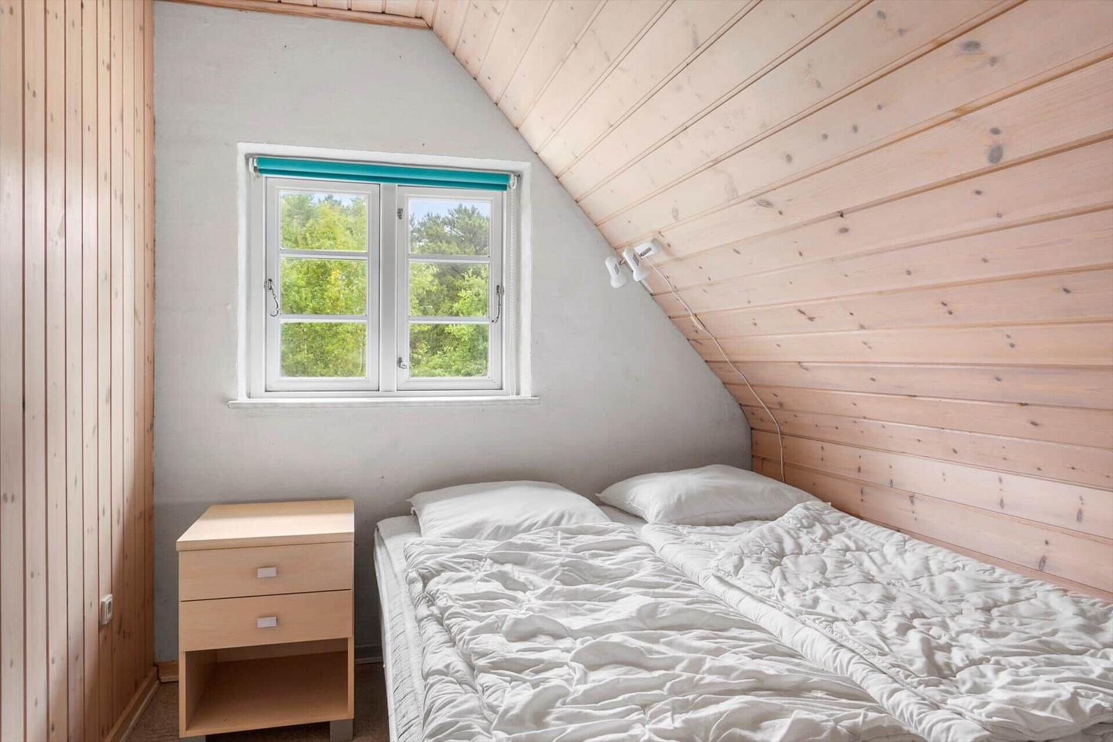 Schlafzimmer mit Dachschrägen, Fenster und Bett.