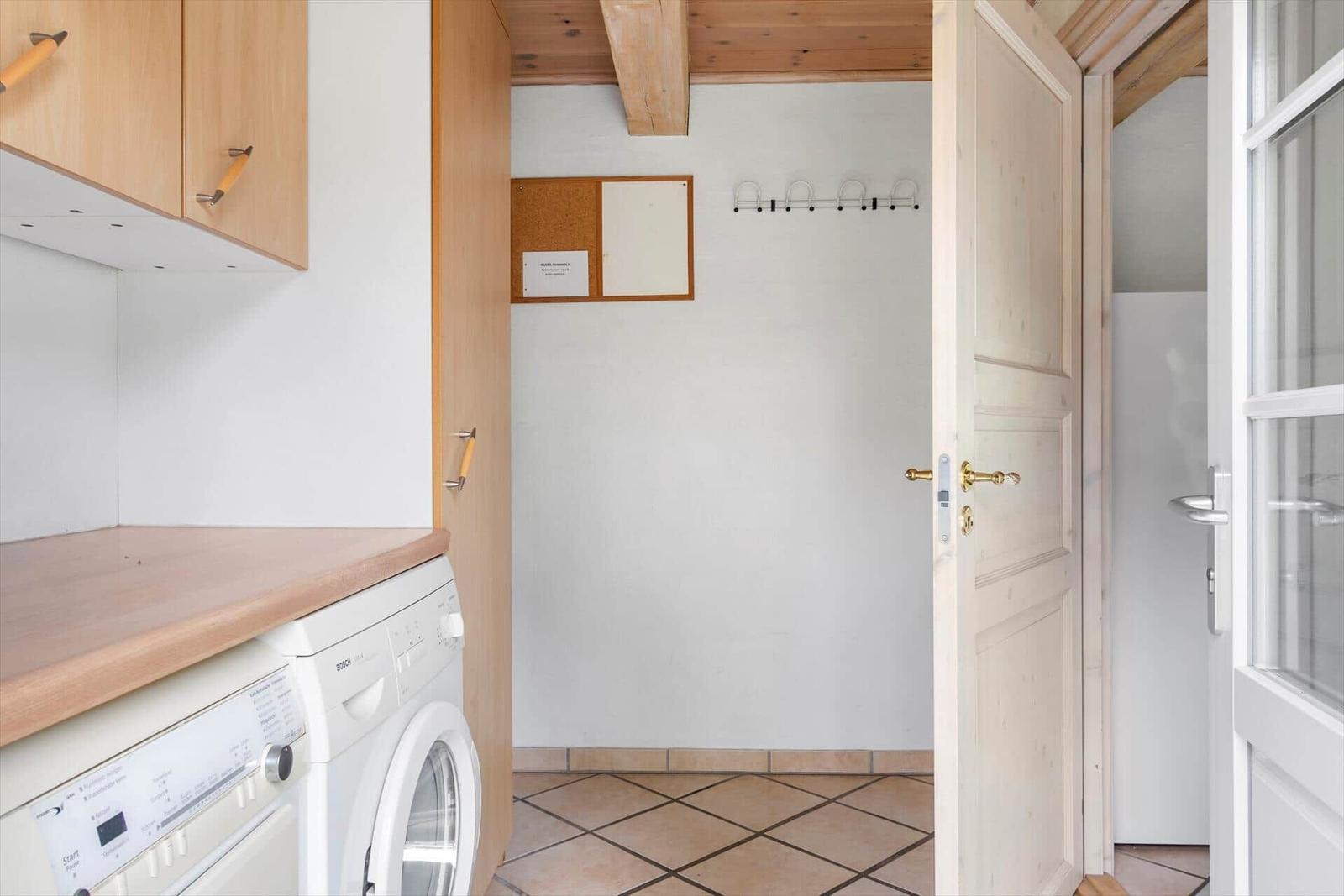 Waschmaschine in Küche mit Holzregalen und Türöffnung.