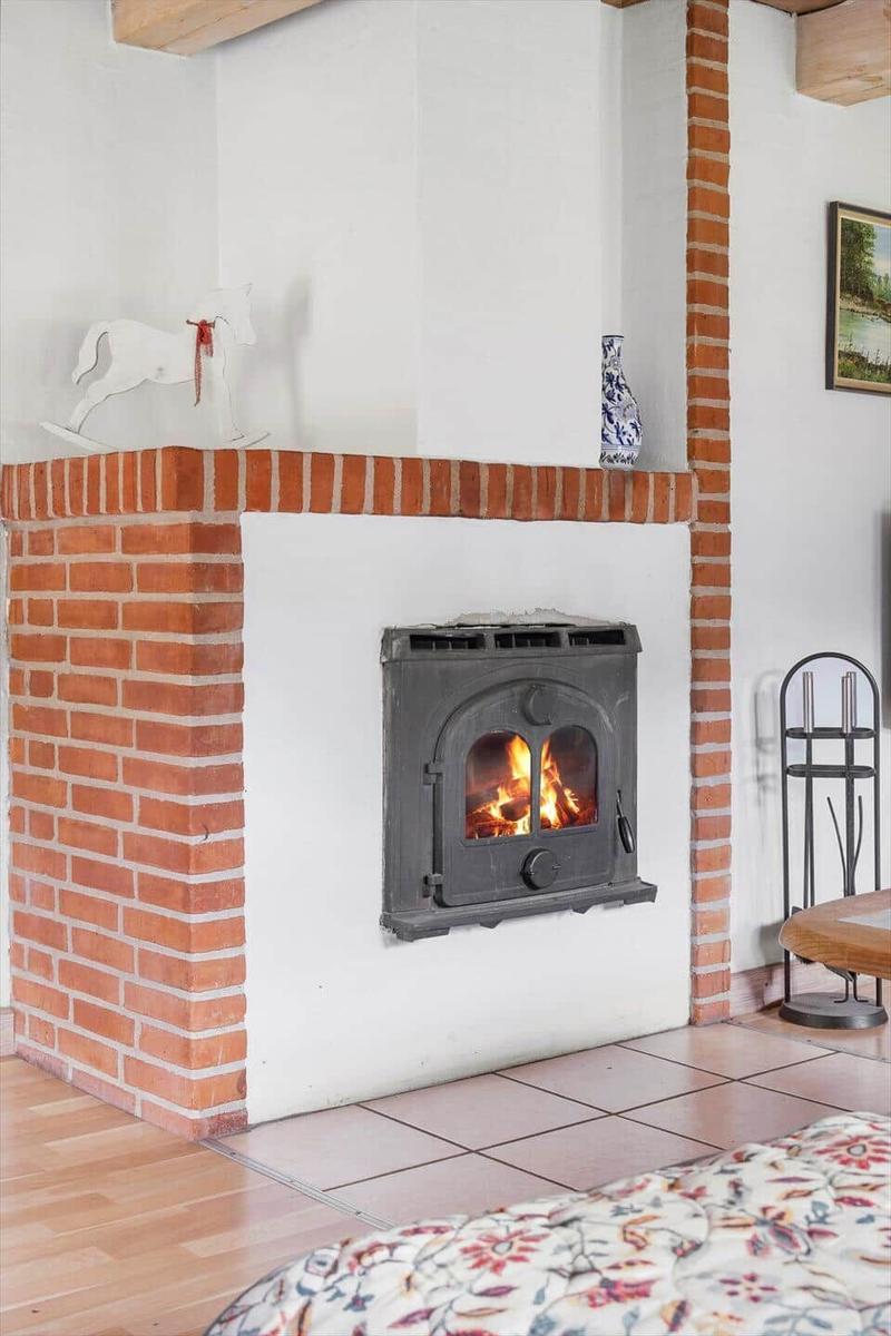 Kamin mit brennendem Holzofen, roter Ziegelsteinmauer und dekorativen Gegenständen.