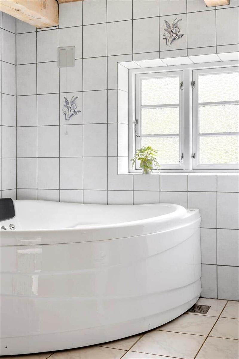 Eine Badewanne in einem Badezimmer mit Fliesenwand und Fenster.
