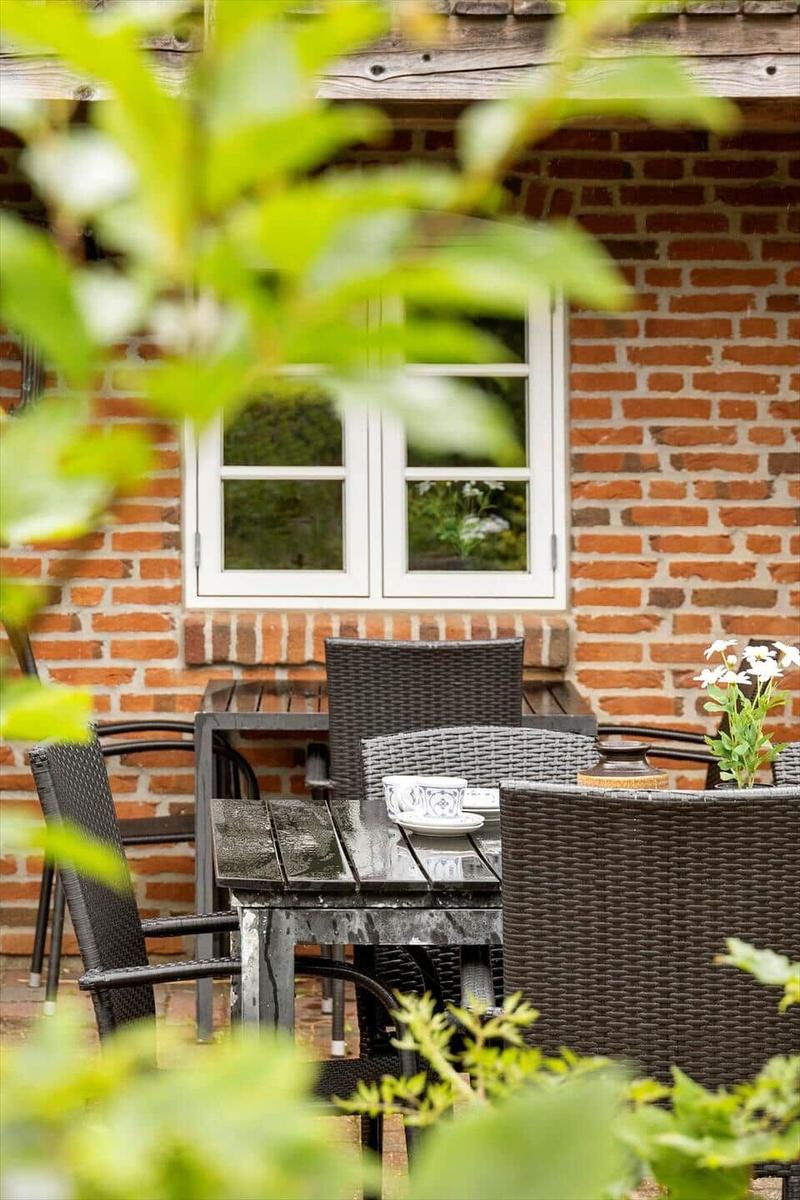 Terrasse mit Tisch und Stühlen vor Backsteinhaus mit Fenster