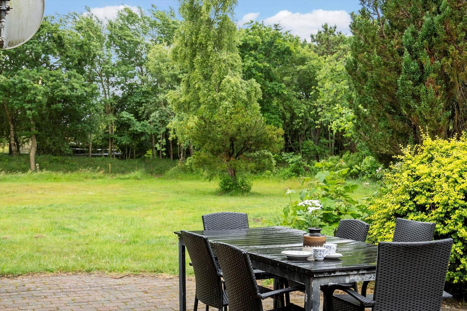Terrasse mit Tisch und Stühlen, umgeben von Grünfläche und Bäumen.