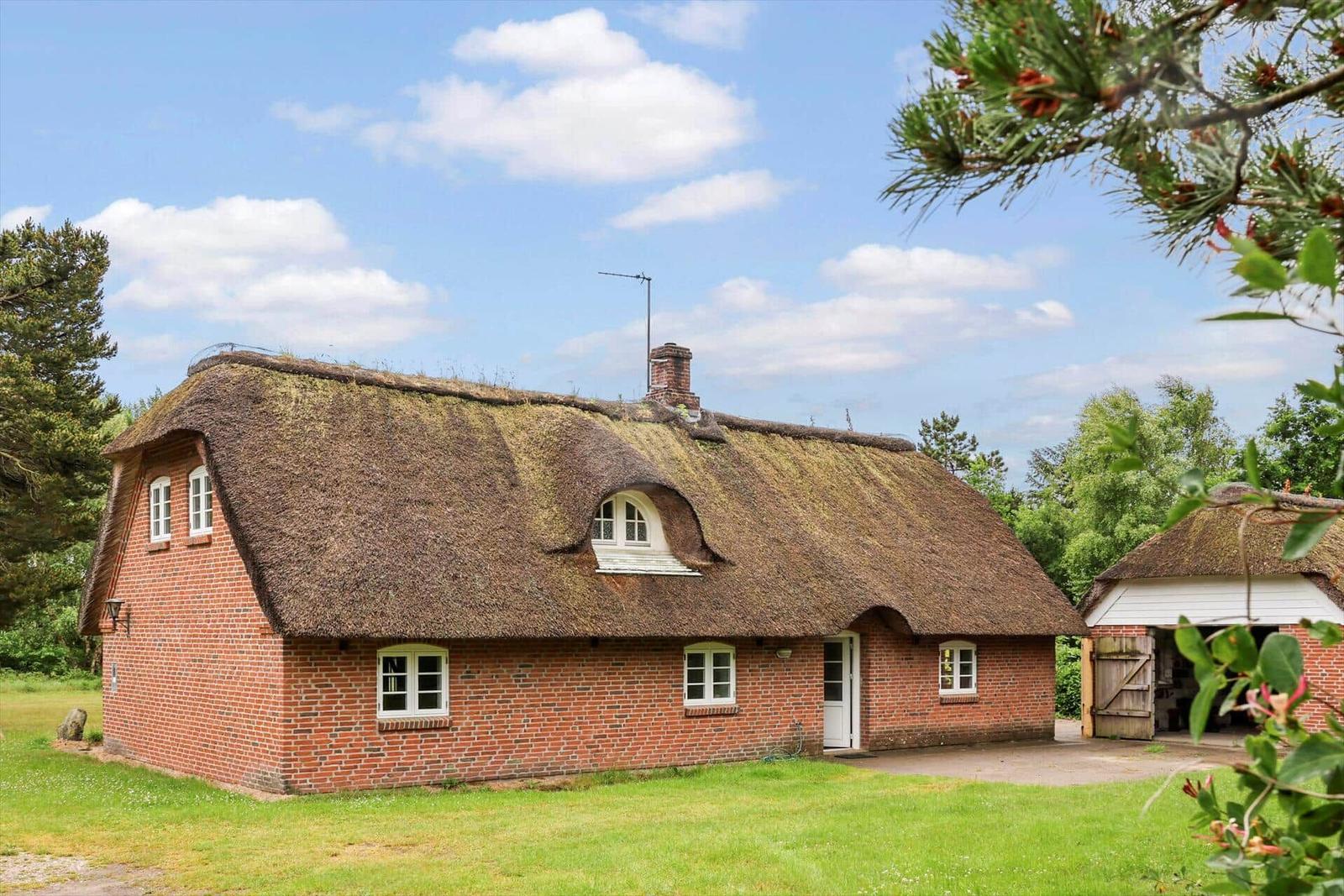 Rotes Backsteinhaus mit strohgedecktem Dach und weißen Fenstern in grüner Umgebung.