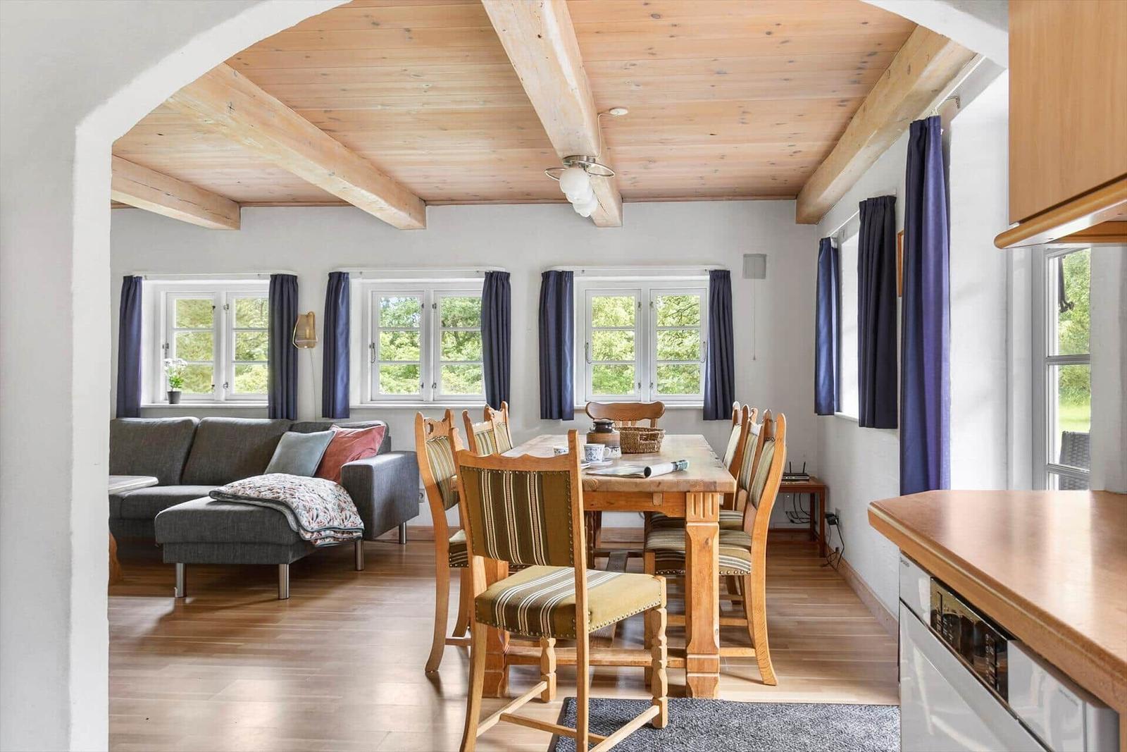 Ein Raum mit Essbereich, Sofa und Holzboden. Holzdecke mit Balken.