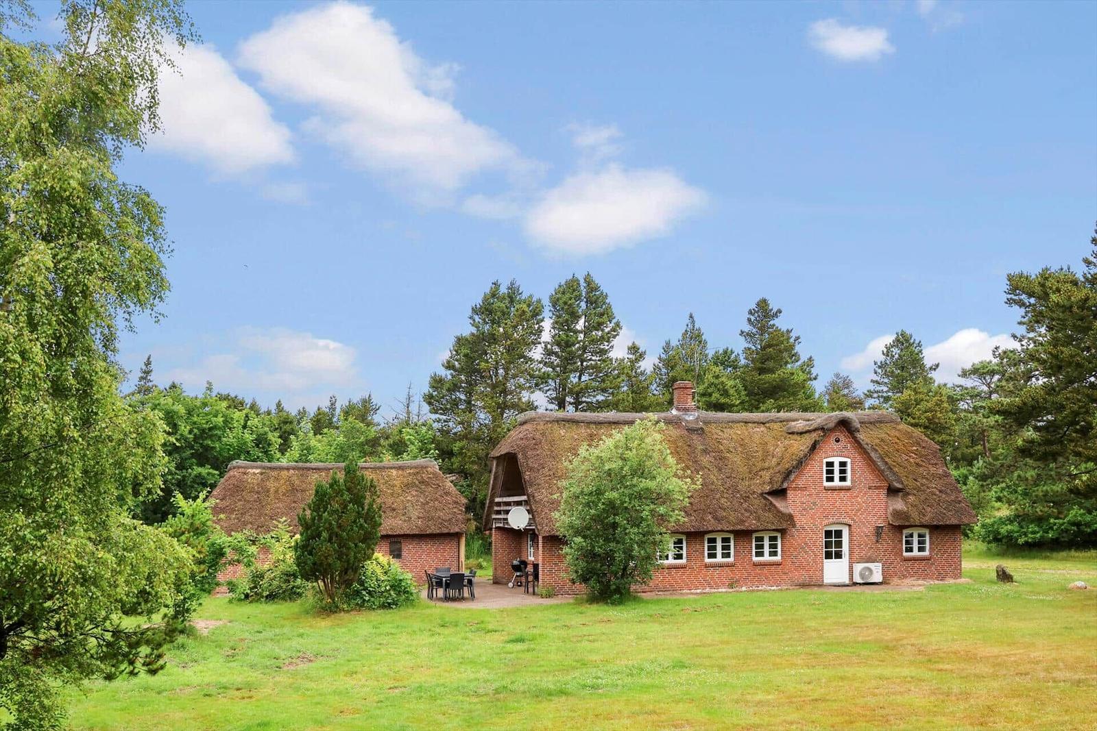Rotes Backsteingebäude mit Strohdach und Garten unter blauem Himmel.