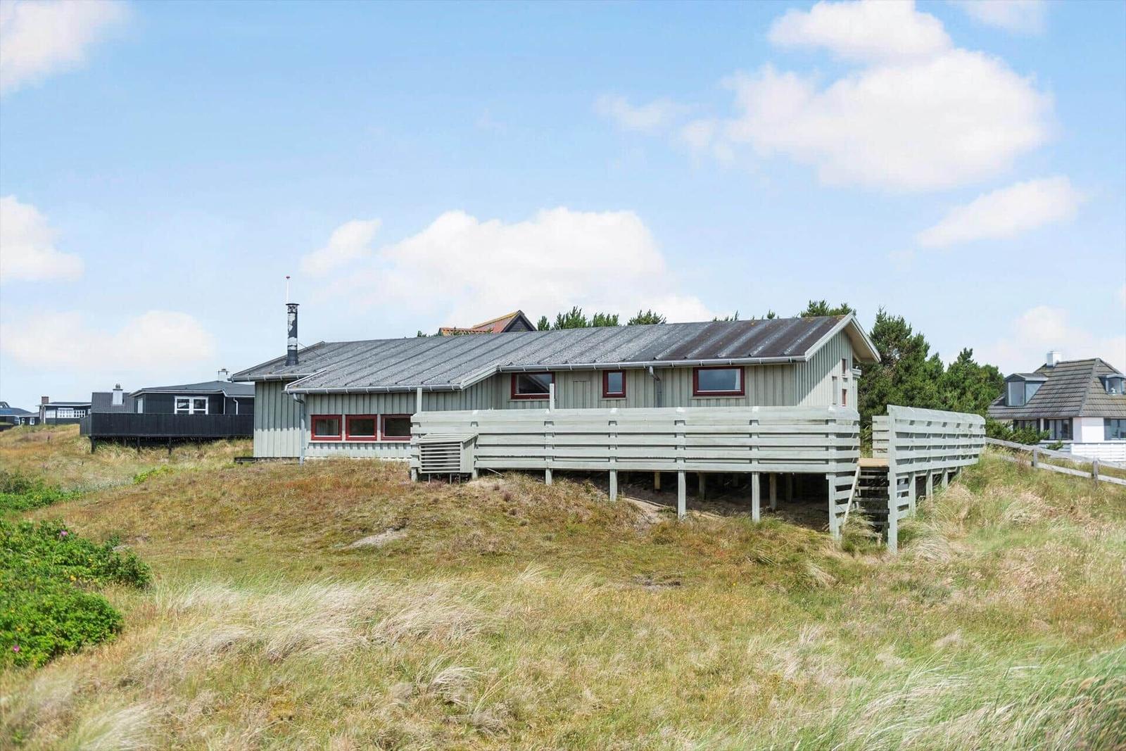 Ein Haus auf einer Düne mit Terrasse und roten Fensterrahmen.