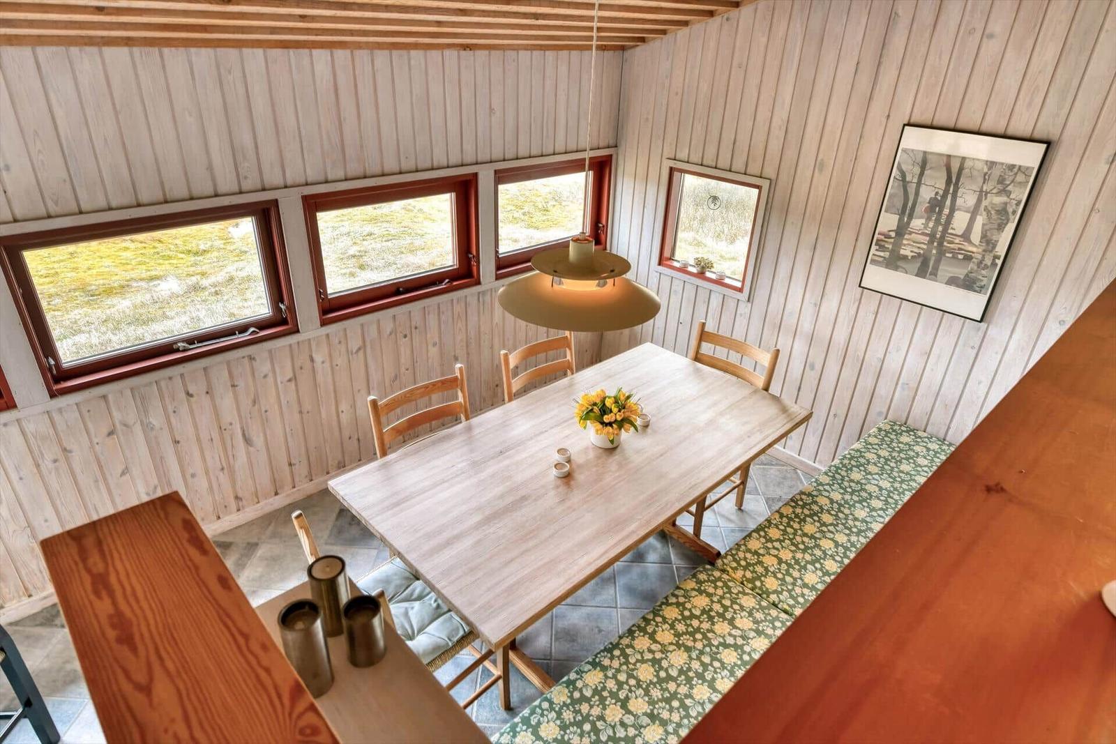 Esszimmer mit Holztisch, Stühlen und Fenstern. Deckenleuchte und Wandbild sichtbar.