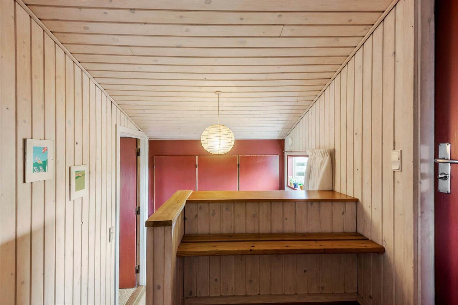 Holzgetäfelte Wand und Decke, hölzerner Sitzbereich, runder Lampenschirm, rote Wand im Hintergrund.
