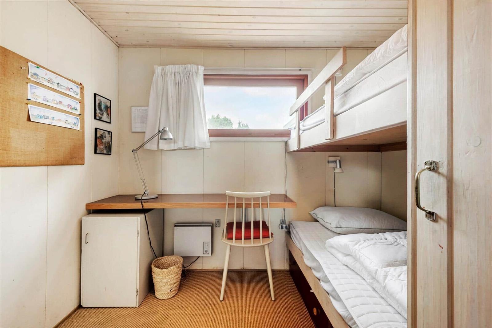 Kleines Schlafzimmer mit Doppelstockbett, Schreibtisch und Fenster.