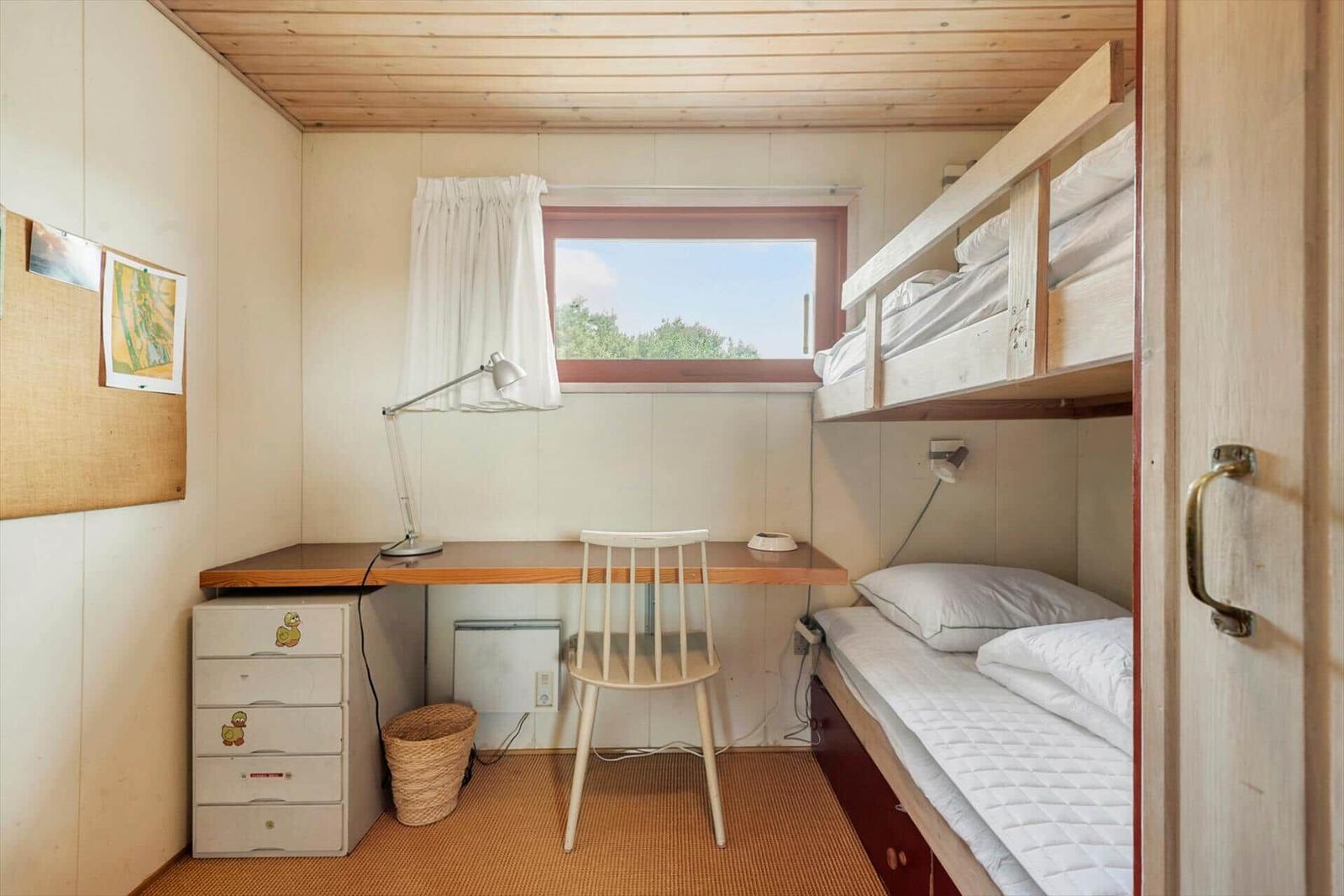 Kleines Zimmer mit Doppelstockbett, Schreibtisch und Fenster mit Blick auf Grün.