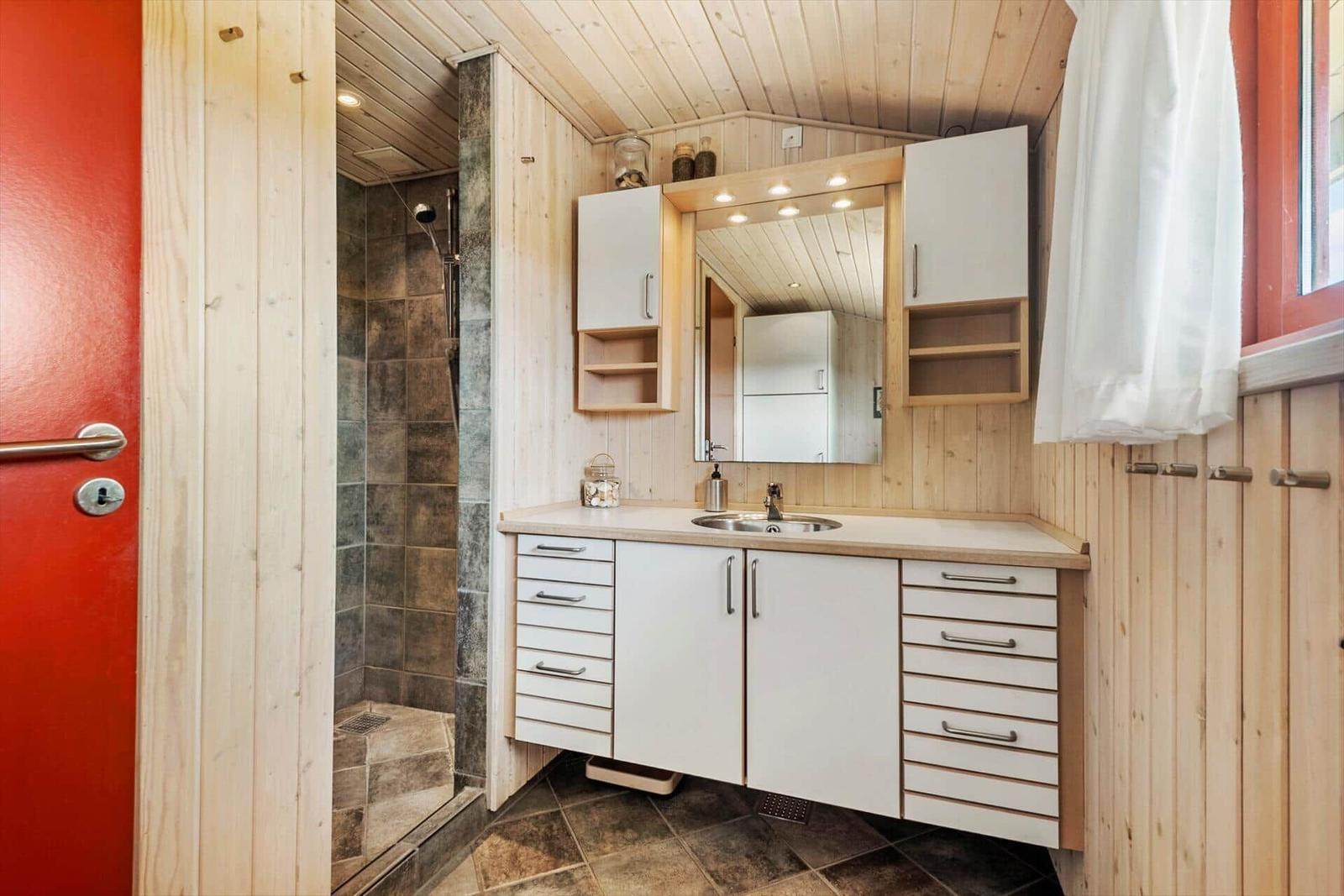 Badezimmer mit Dusche, Waschbecken und Spiegelschrank. Holzwände und Fliesenboden.