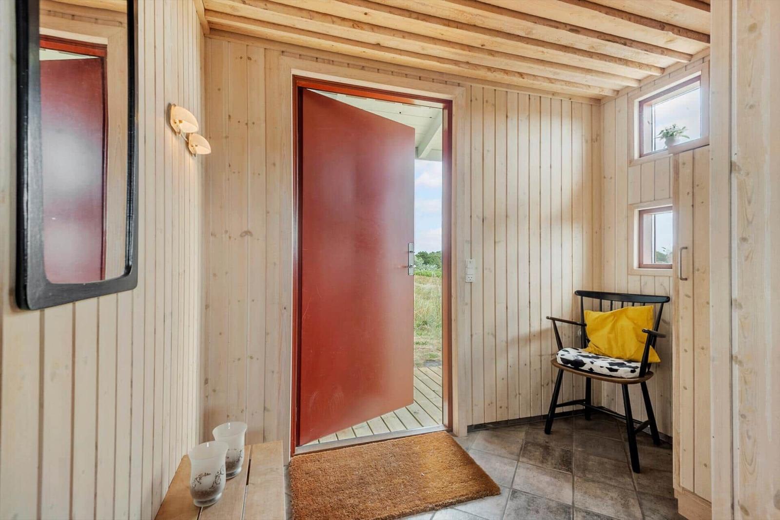 Eingangsbereich mit Holzwand, roter Tür und Stuhl mit gelber Kissen.