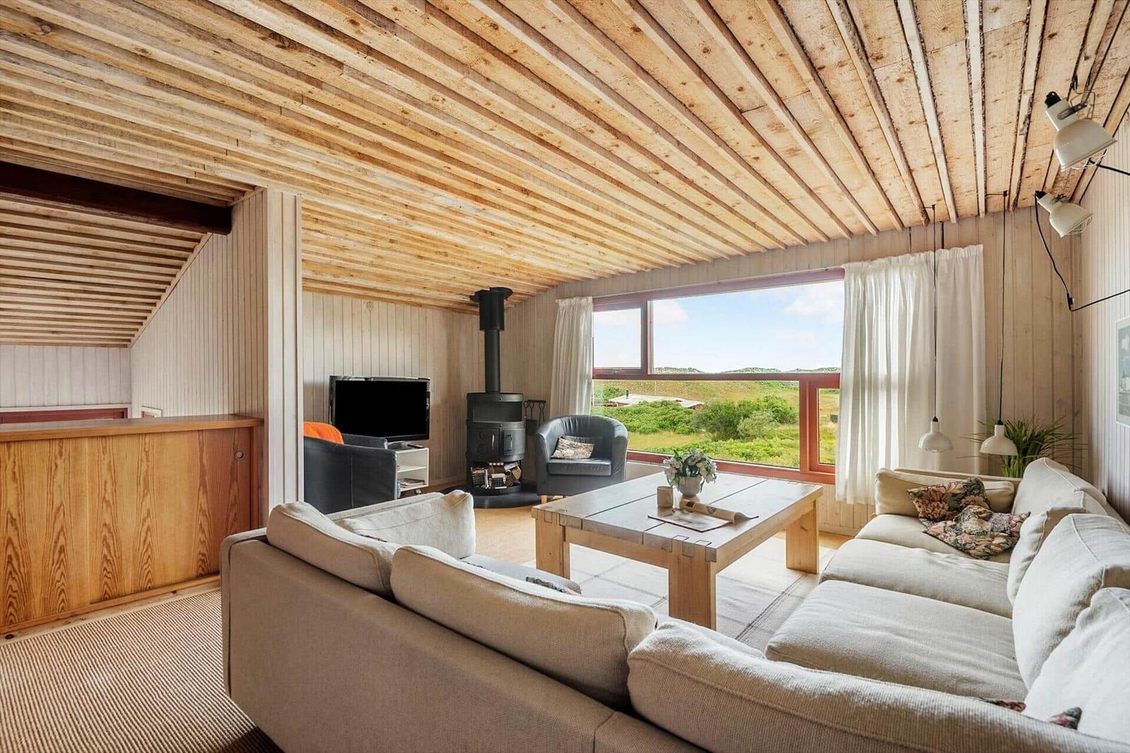 Wohnzimmer mit Holzdecke, Sofa, Kamin und Blick auf die Landschaft.