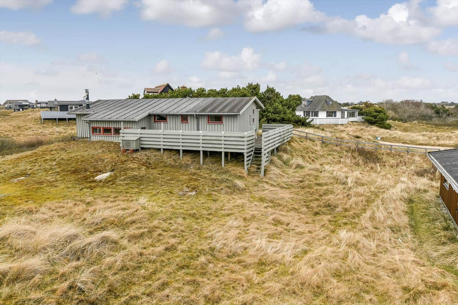 Ein graues Haus mit Balkon steht auf einer grasbewachsenen Düne.