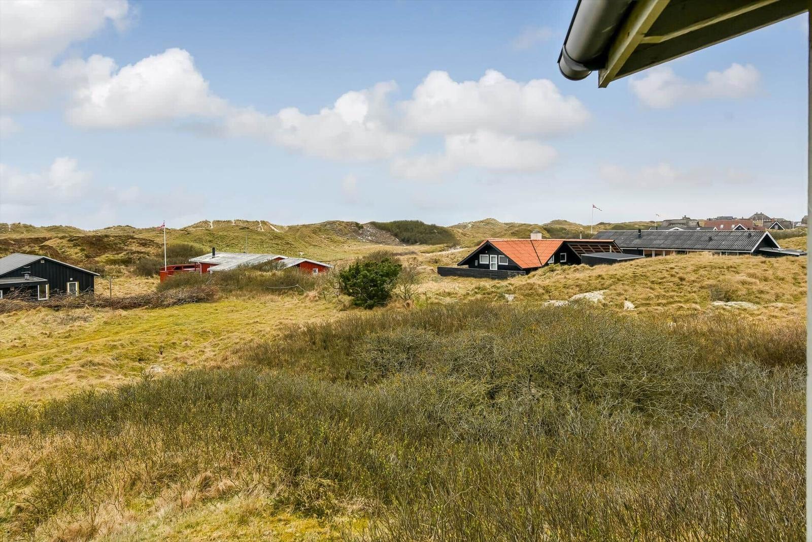 Dorfhäuser auf Dünenlandschaft unter blauem Himmel mit weißen Wolken.