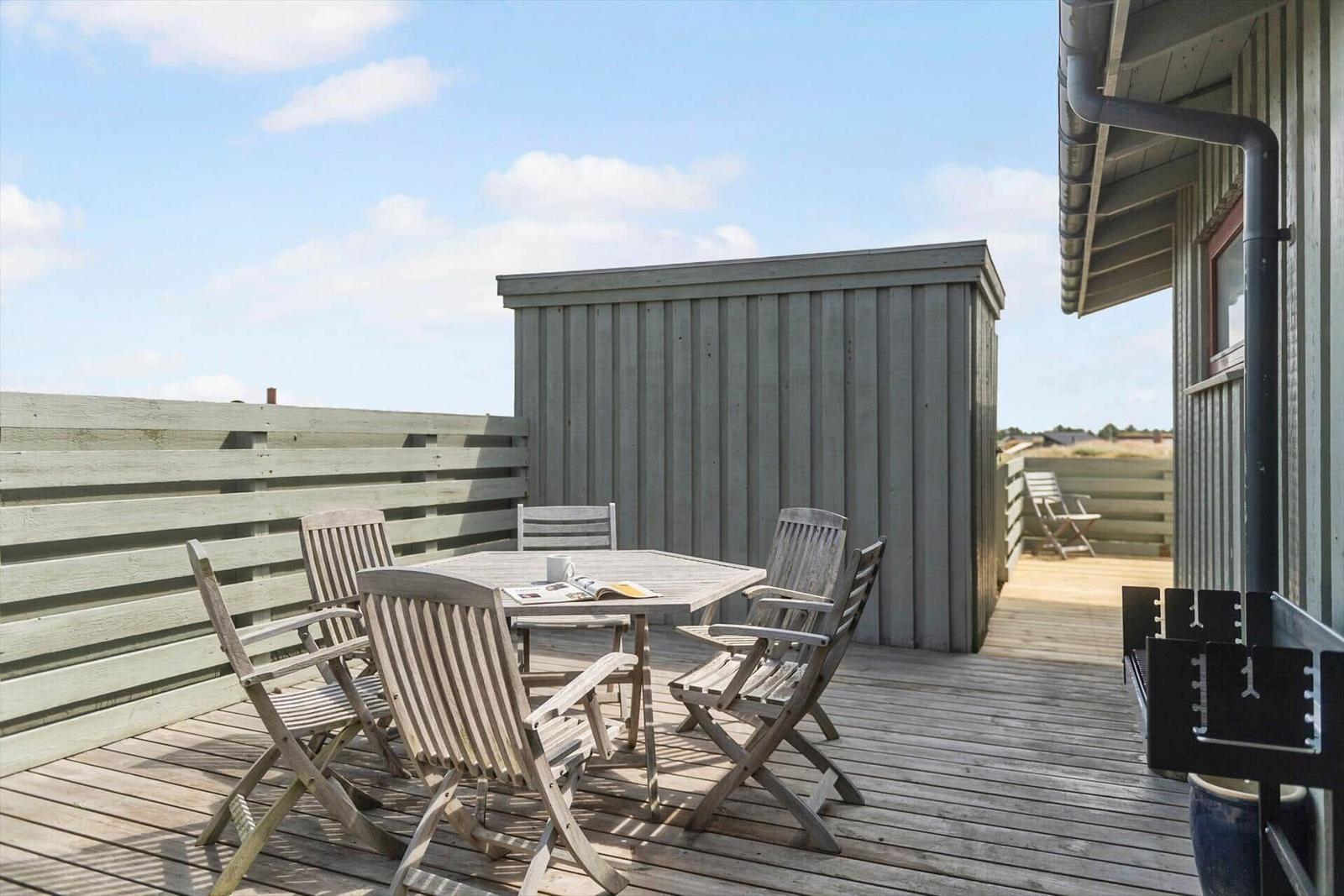 Terrasse mit Holztisch und Stühlen, Holzwand und kleinem Gartenhaus.