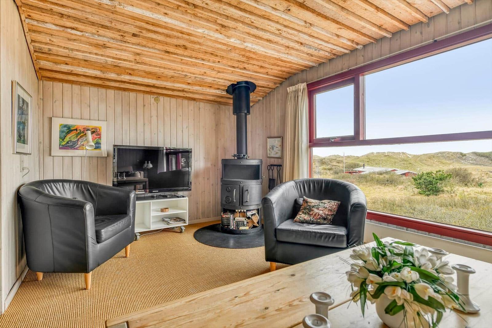 Wohnzimmer mit Holzdecke, Kamin und großem Fenster mit Aussicht.