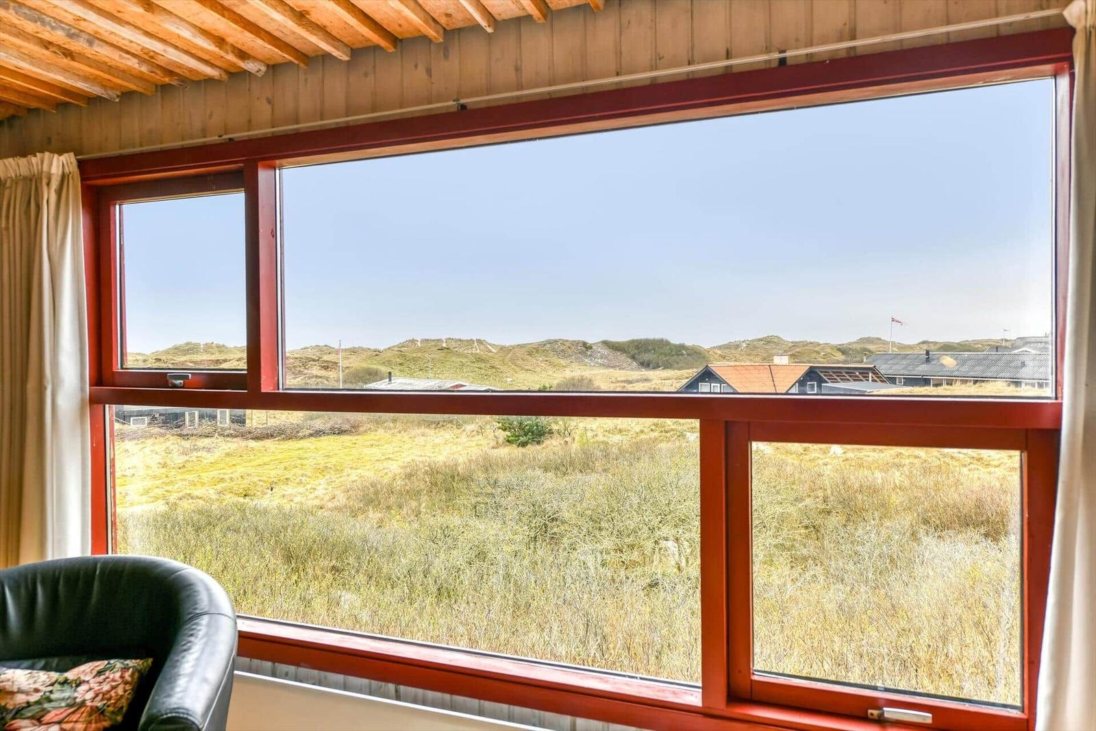 Roter Fensterrahmen mit Blick auf Dünen und Häuser.