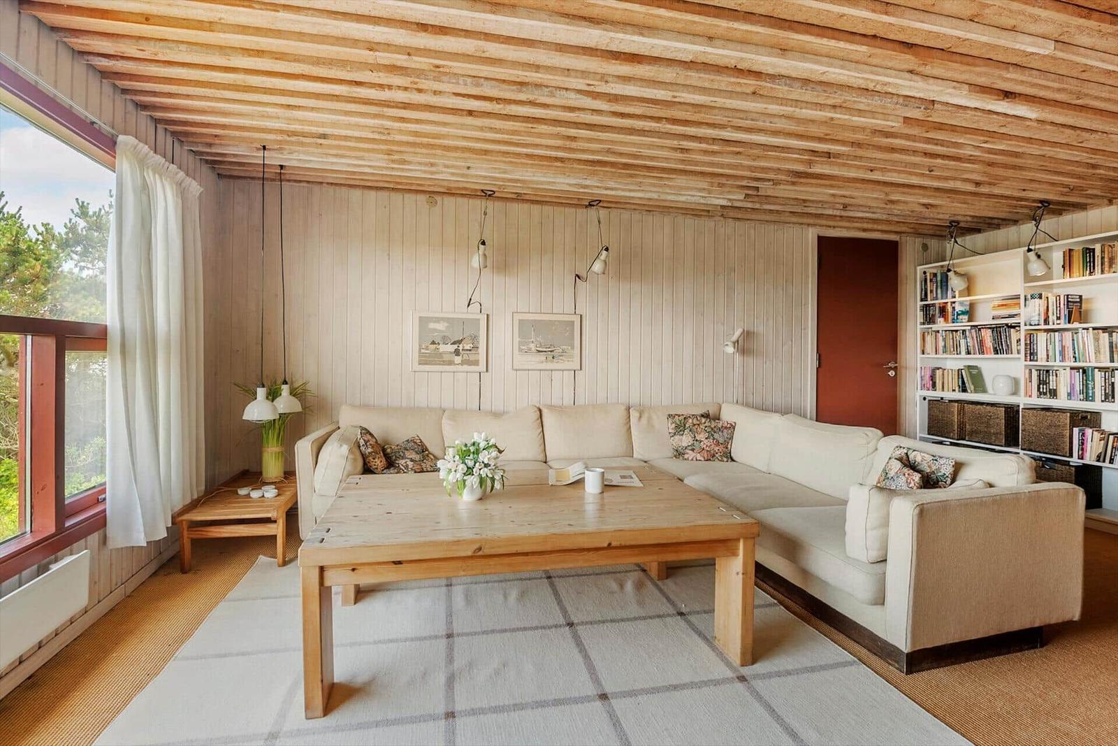 Wohnzimmer mit Holzdecke, Sofa, Tisch und Bücherregal.